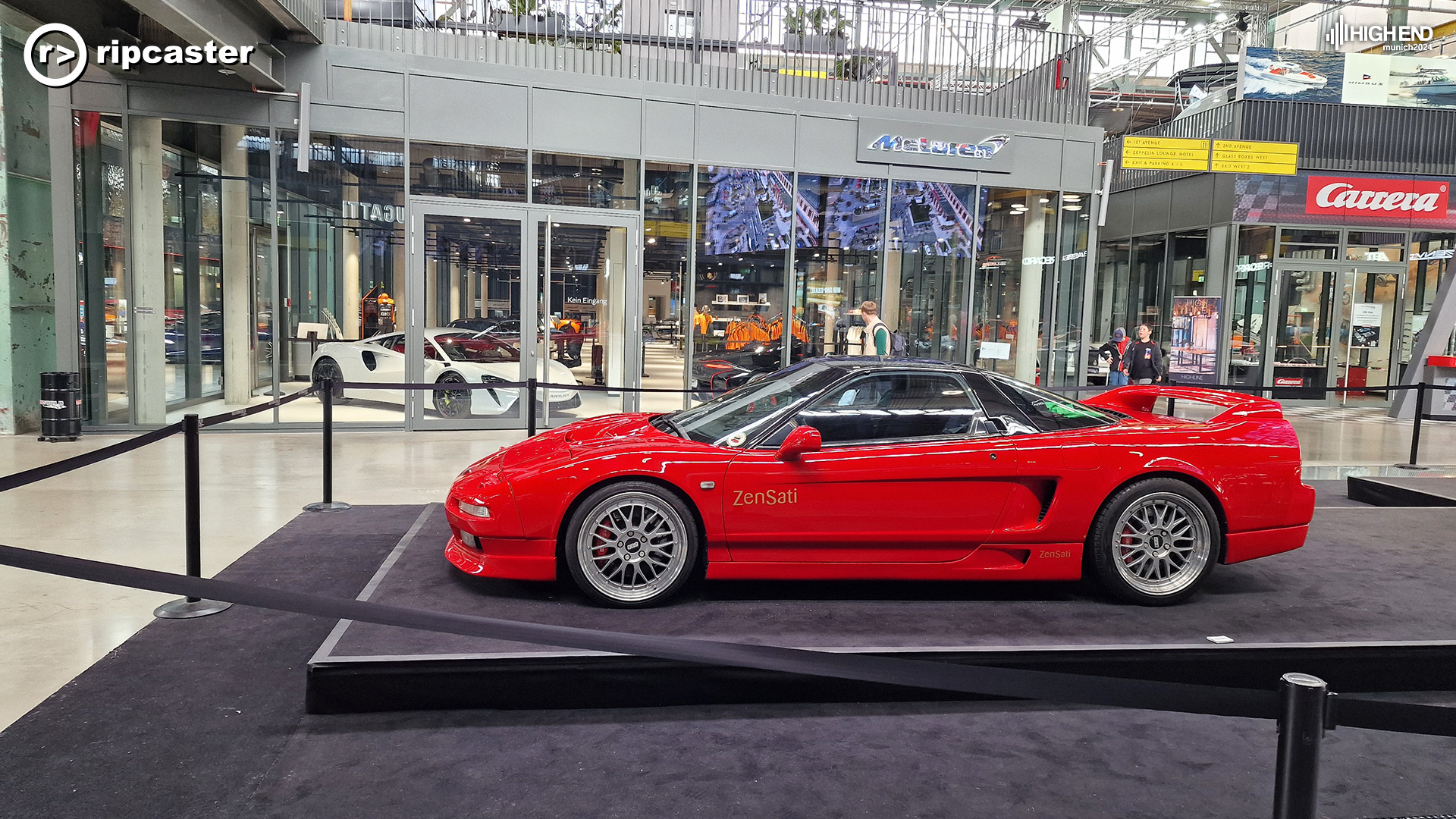 A red sports car in front of glass rooms with other sports cars inside