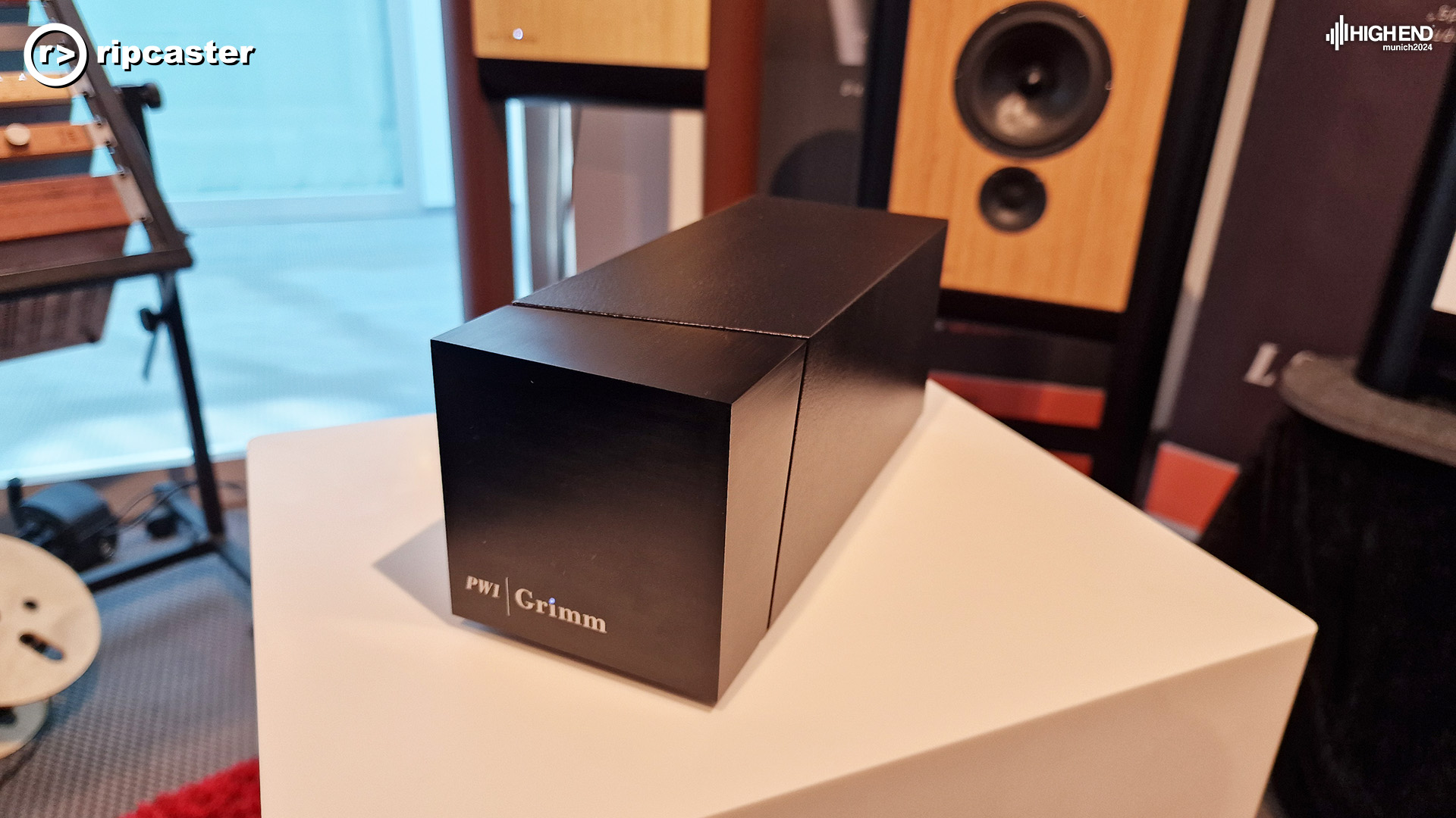 The Grimm PW1 which is a long rectangular box shape.  There are speakers in the background .  The Grimm speakers are thing rectangular shaped with legs either side of the rectangle.