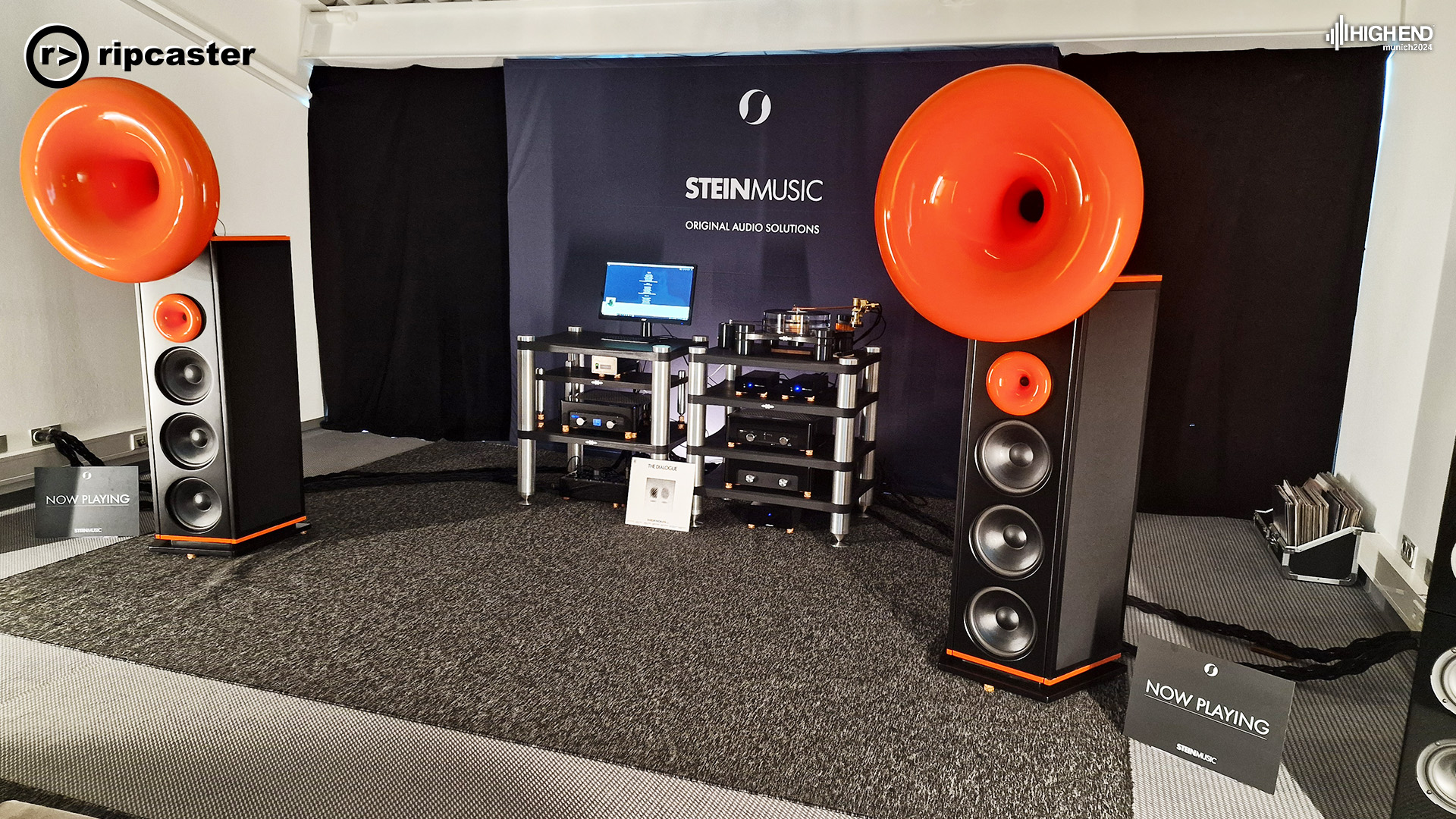 A pair of floorstanding speakers with HiFi kit between.  Stein Music.  The speakers have orange trumpets on the top