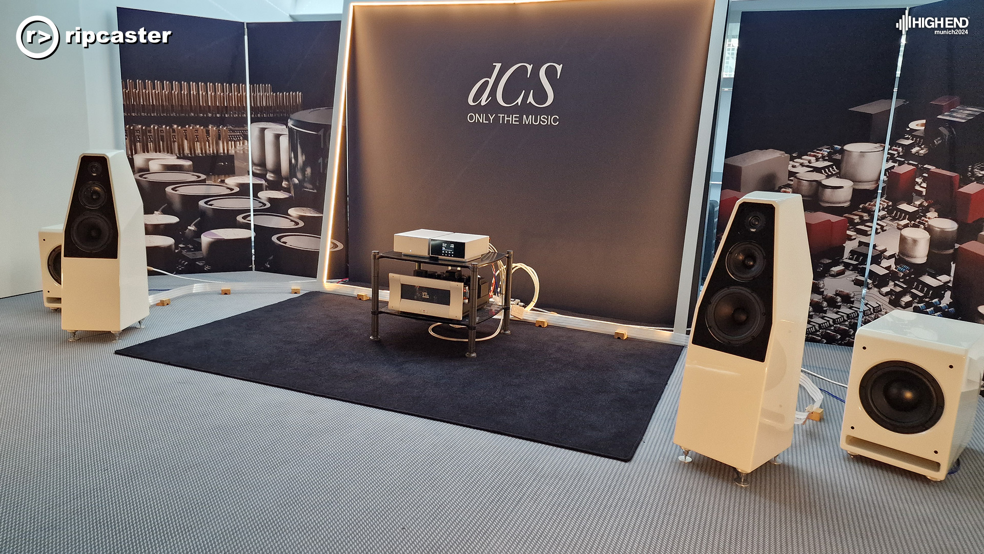 dcs.  A pair of floorstanding white and black speakers with other pieces of hifi equipment between