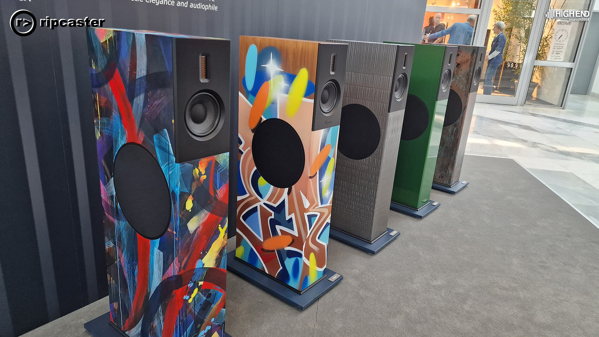 The same style of floorstanding loudspeaker lined up each one is a different colour.  Two of them have very colourful patterns on.