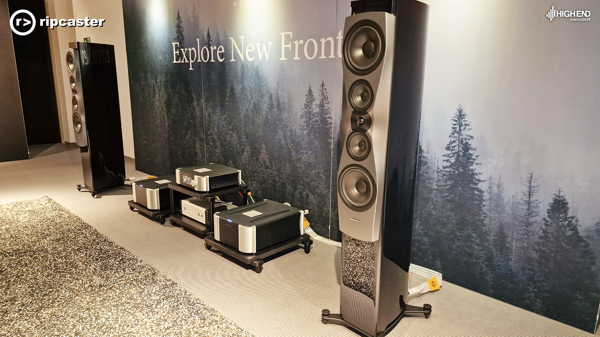 MOON  equipment between two large floorstanding speakers.  The backdrop is a forest with the words "explore new frontiers"