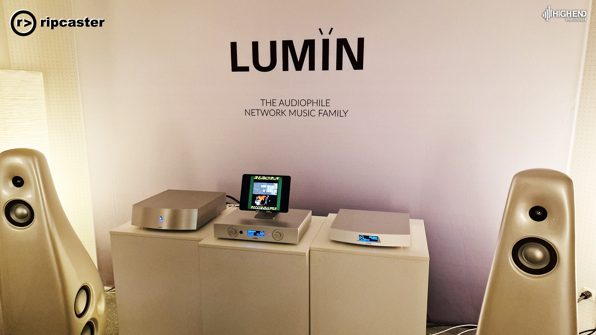 Three pieces of Lumin equipment between a pair of speakers.  The middle one has an  iPad on a stand on top of it