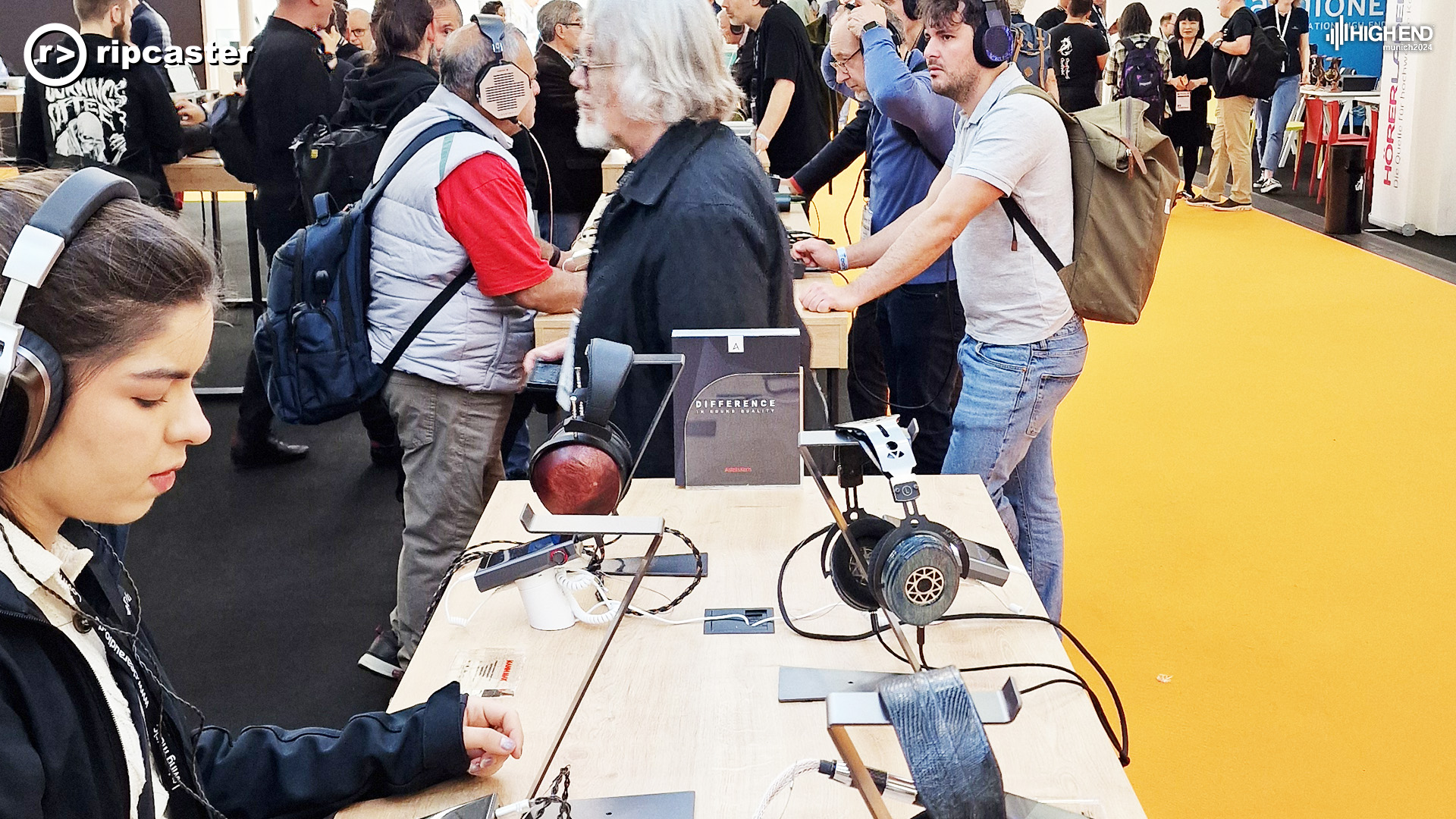 A young woman in the foreground wearing headphones.  Lots of people in the background of the photo also wearing headphones and some looking around generally