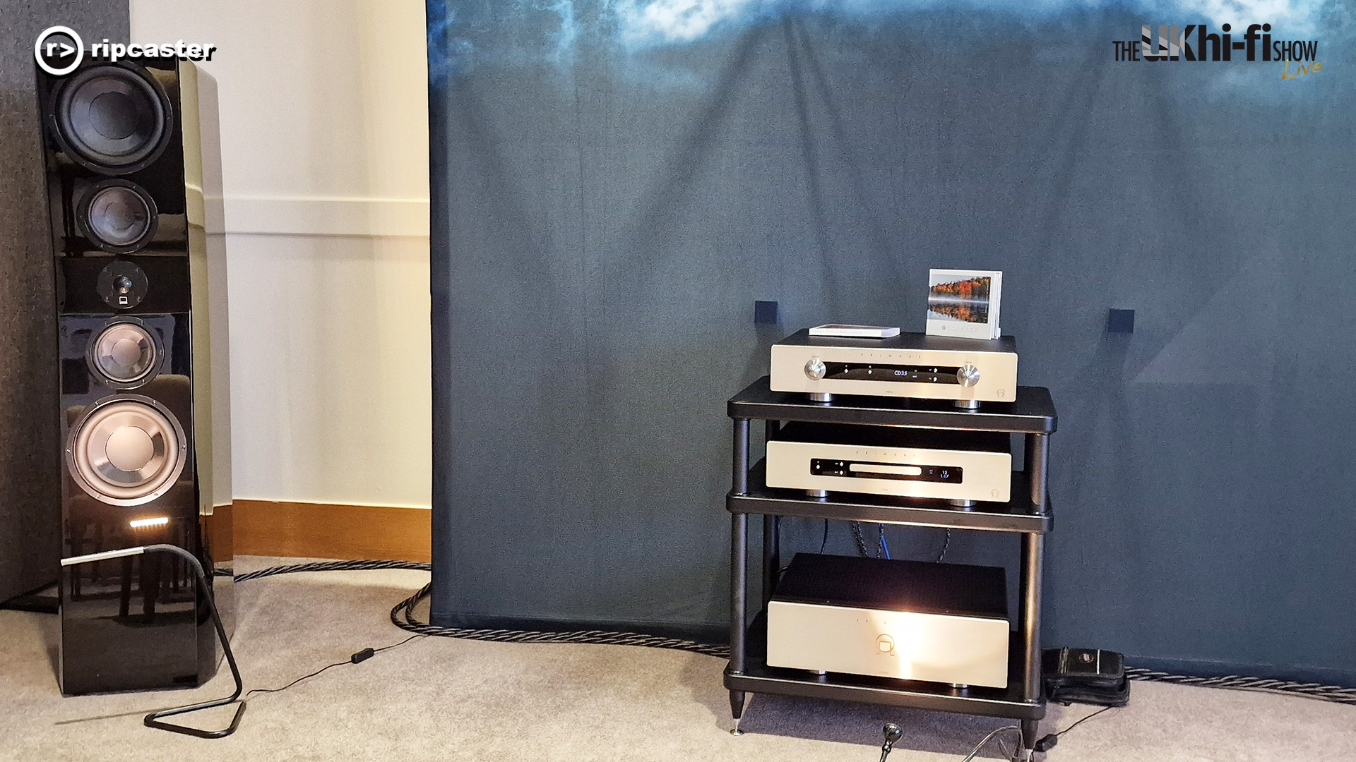 A black floorstanding speaker to the left and a rack of HiFi equipment in the centre