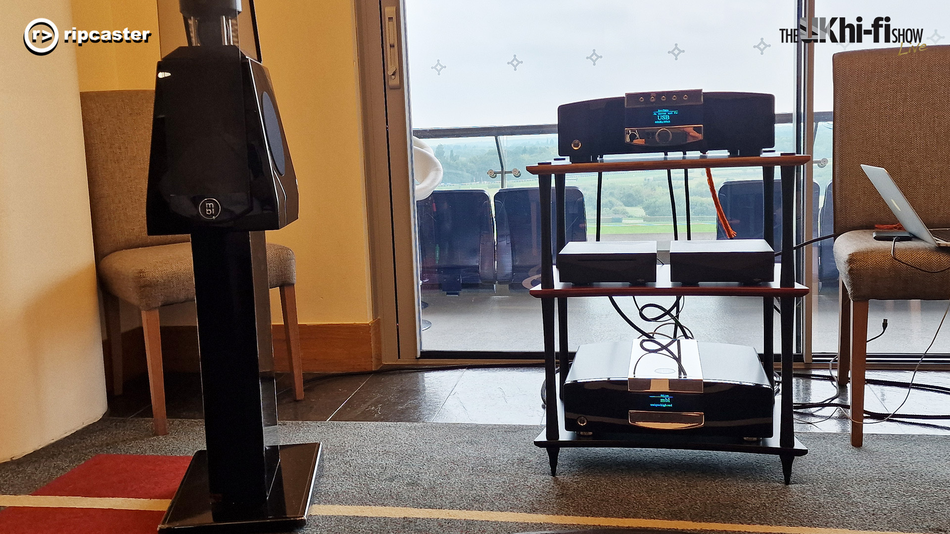 A black speaker on a stand beside HiFi equipment on a stand