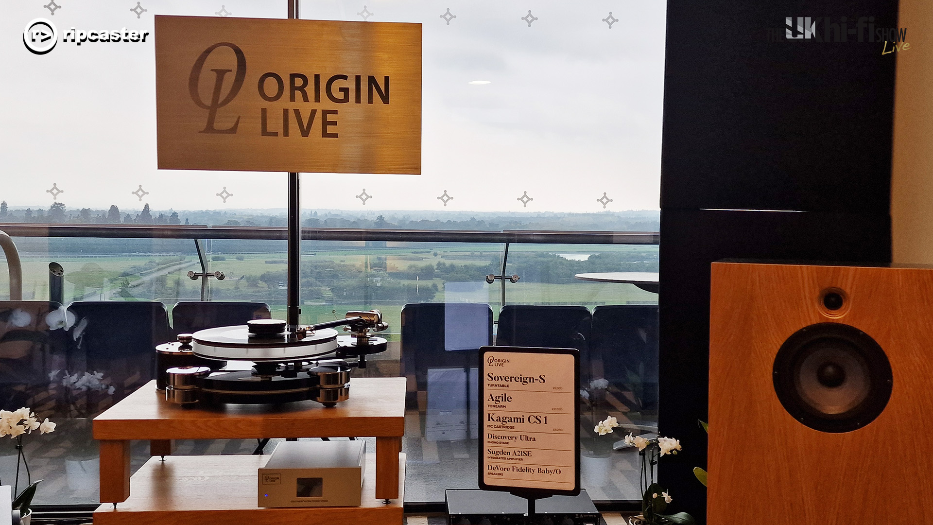 Origin Live.  A wooden speaker to the right and a turntable to the left.  The background is a view over the racecourse