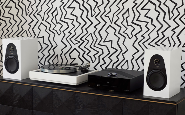 Linn 119 Loudspeakers in white on a side unit with a DSM and an LP12.  the wallpaper in the background consists of lots of black zigzag lines on a white background