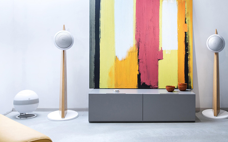 A pair of Cabasse Baltic 5 speakers in white on stands either side of a low unit with abstract art behind.  A cabasse sub on the floor.