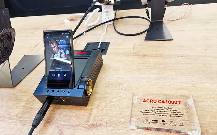 Astell & Kern ACRO CA1000T with an A&K player stood up in it.  It's on a wooden table with some headphones partly visible on the left.