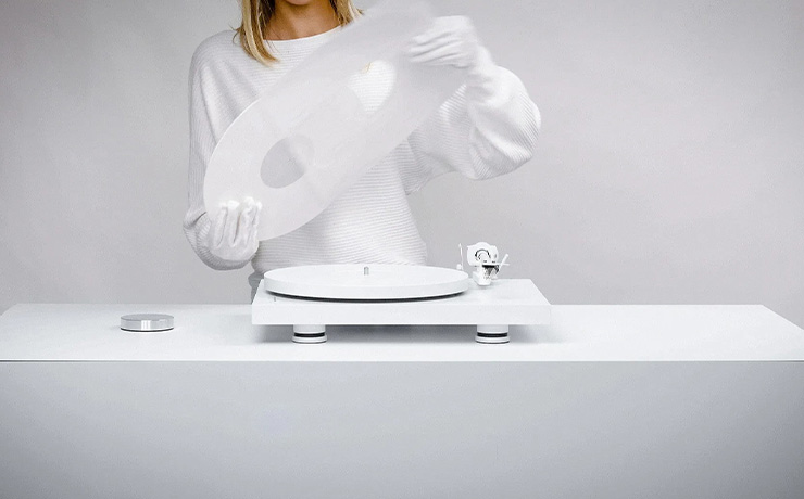 Project Debut PRO B Turntable White Edition on a white table with a woman standing behind it.  She's removing a white record from a white record sleeve