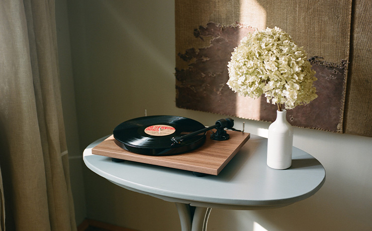 Project E1 Turntable in Walnut on top of a small table with a vase of hydrangea beside it