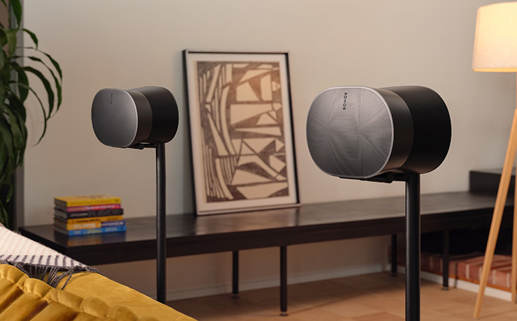 A pair of Sonos Era 300 speakers in black on black stands behind a sofa in a living space