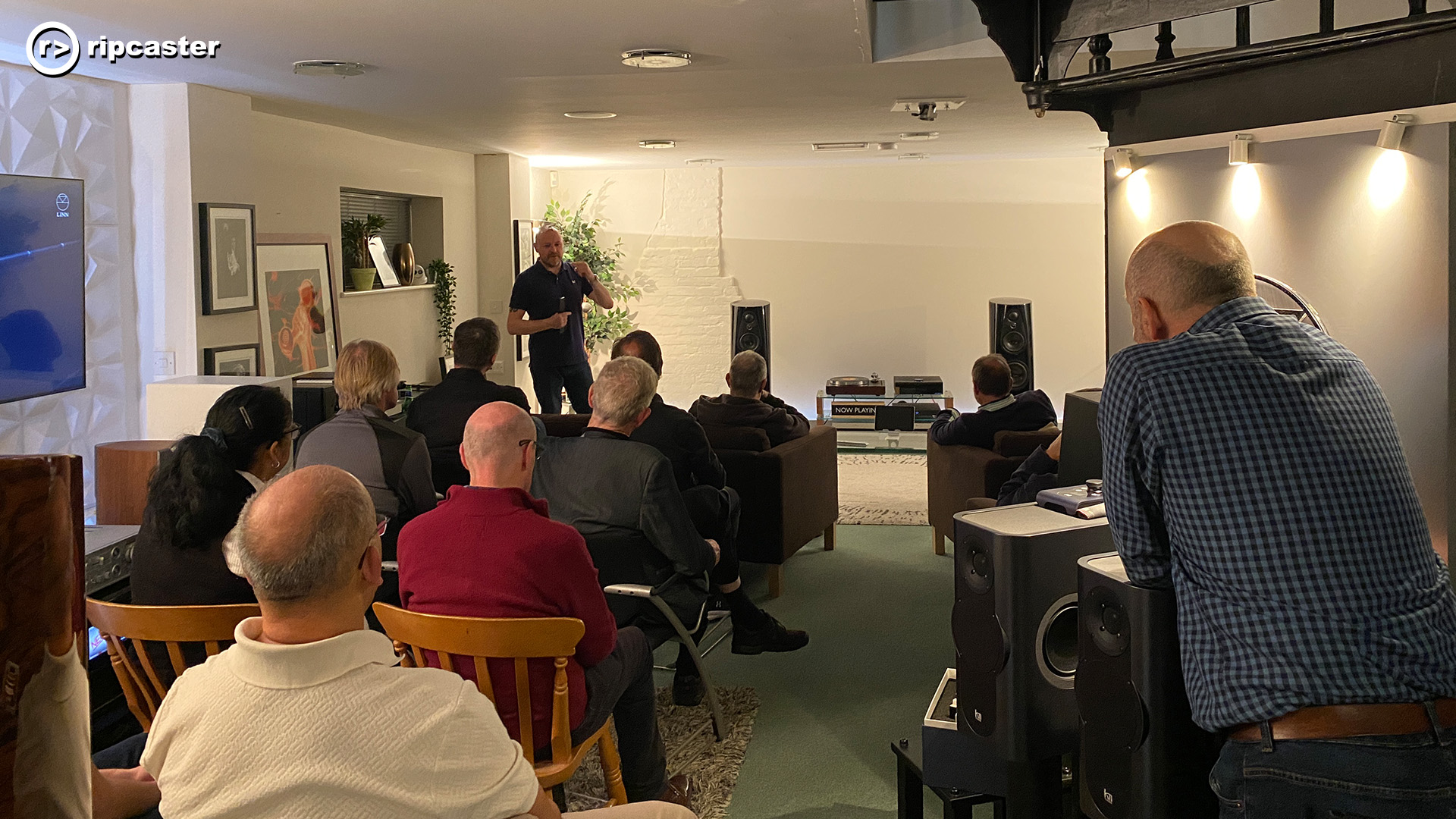 A room full of people viewed from the back with one person speaking to the group who can be seen facing the direction of the camera