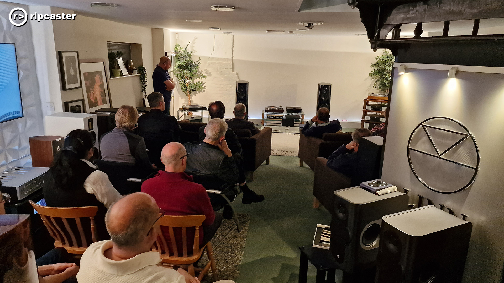 A room full of people facing away from the camera looking towards a HiFi system