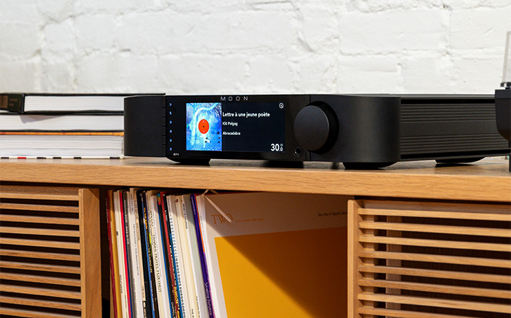 The Moon 371 on a wooden unit with books stacked beside it. Underneath in the unit is vinyl standing up on a shelf