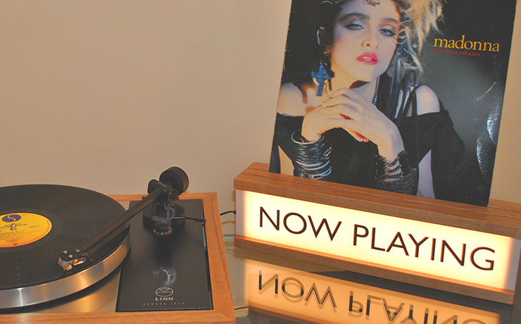 Now Playing sign with a Madonna album in the groove space at the top.  There's an LP12 to the left of the sign