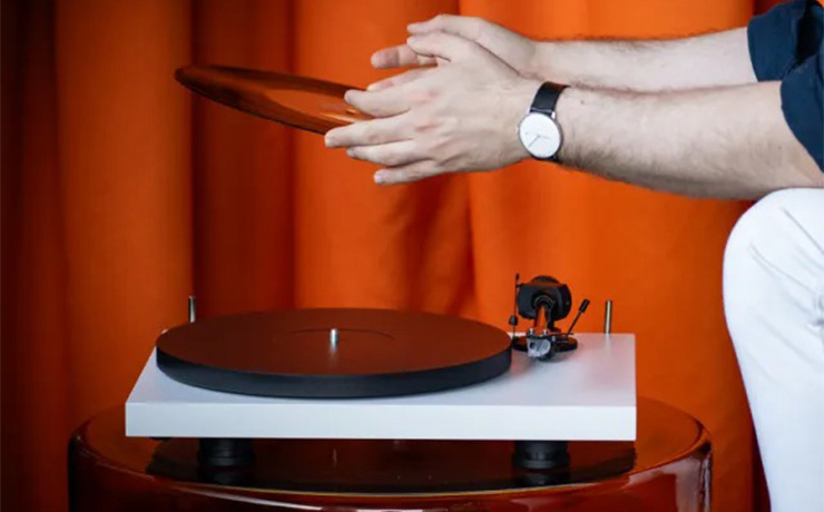 The Project EVO 2 turntable in white with a man sitting beside it holding a record.  There's a dark orange curtain in the background