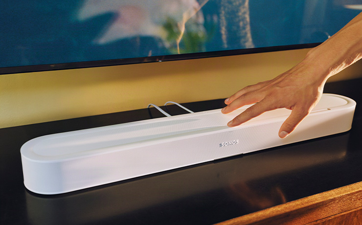 SONOS Beam Ultra in white on a low side unit with a hand adjusting a control