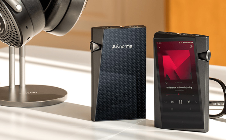 A pair of Astell & Kern A&norma SR35 Portable Music Players standing up beside some headphones on a stand