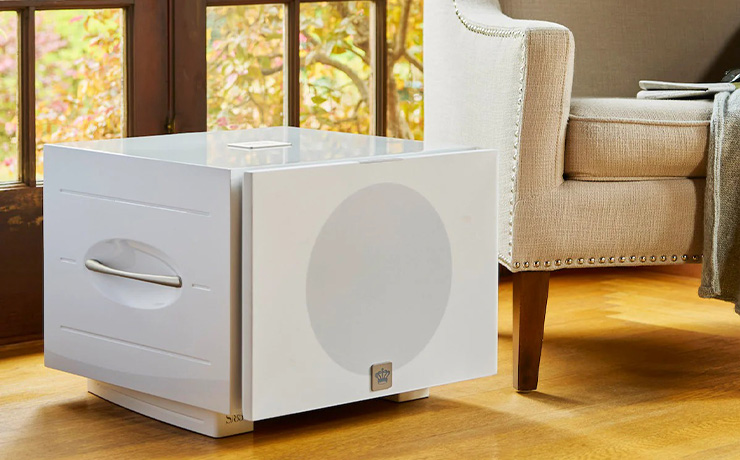 A white REL S/850 on a wooden floor in a living space.  The grille is cloth