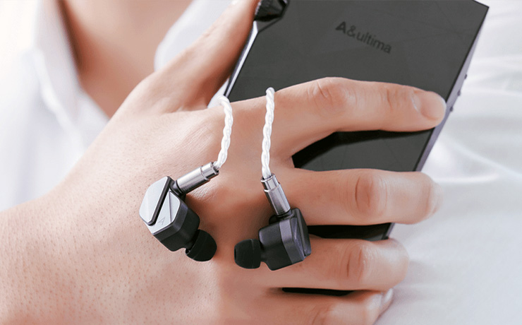 Astell & Kern Zero 2 earphones hanging over the hand that's holding the Astell & Kern music player
