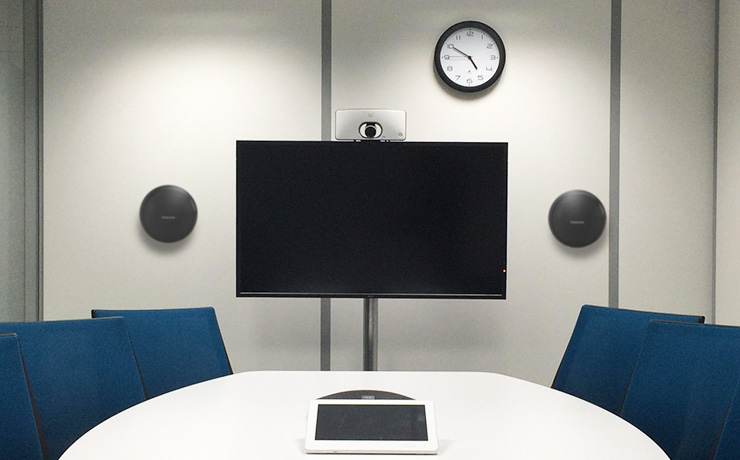 a pair of Cabasse Riga 2 speakers either side of a tv screen in a meeting room with a clock on the wall