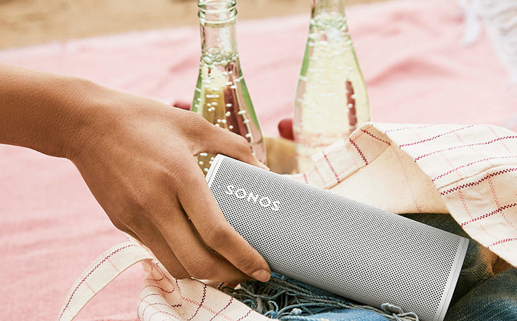 Sonos Roam in white being put into a bag with two bottles of lemonade beside the bag