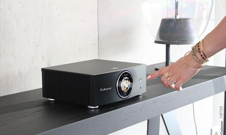 Cabasse Abyss Stereo Amplifier on a side table with a woman's hand reaching for the controls.