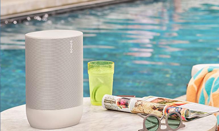 Sonos Move in white on a table with a drink, magazine and sunglasses.  there's a swimming pool in the background
