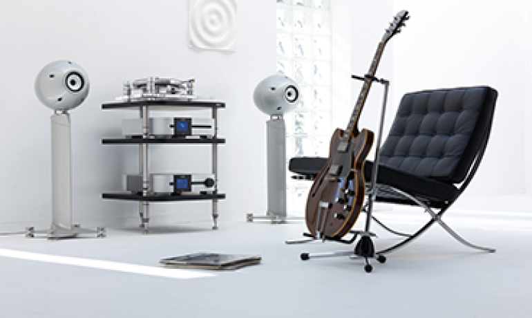 A pair of Eclipse TD712zMK2 with a hifi between in a white room with a guitar propped beside a chair.