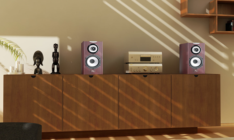 A pair of Cabasse Minorca Loudspeakers on a wooden sideboard with a stereo between them.