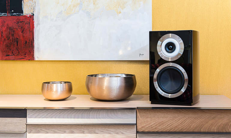 Cabasse Murano speaker on a side-board beside two bowls.  The wall in the background is yellow.