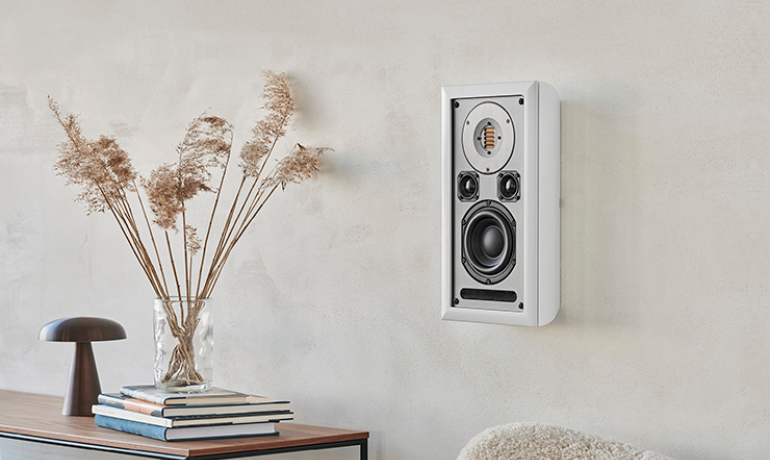 Audiovector OnWall Speaker.  There's a table with a vase that's standing on top of a stack of books which are on top of a table to the left of the image.  There's also a wooden large mushroom to the left of the book stack.