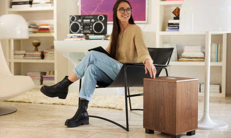 REL Classic 99 Subwoofer in a living space with a woman sat on a chair beside it.