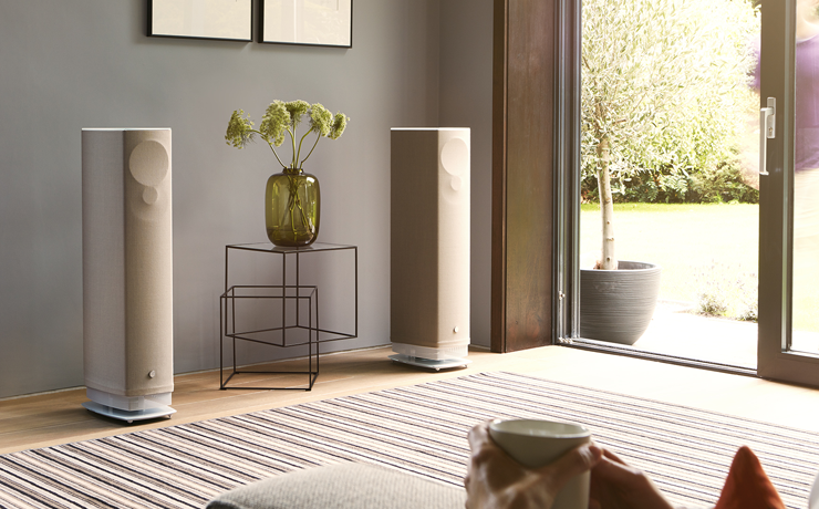 A pair of Linn Series 5 530 Exakt Active Speakers in butterscotch with a table between them and large patio doors to one side.