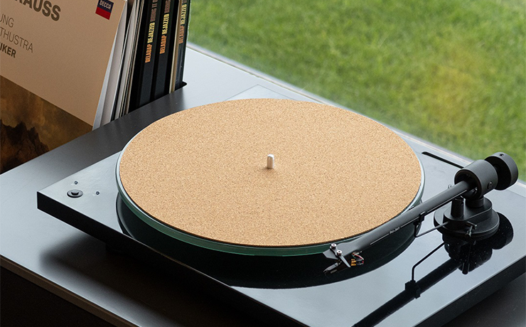 Project Cork-IT 12" cork mat on a turntable with a stack of records beside it.  In front of a window with a lawn visible.