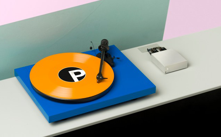 Project Debut Carbon DC Turntable on a grey shelf with an orange record playing