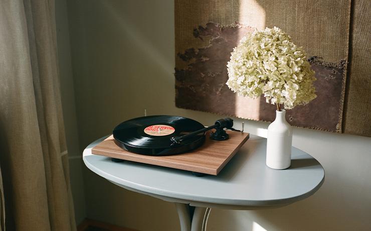 Project E1 turntable in walnut on a small table with a vase of hydrangea beside it