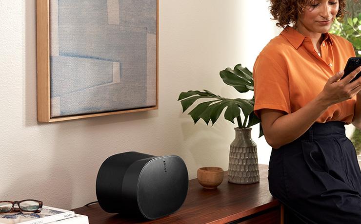 the SONOS Era 300 speaker in black on a wooden side unit with a woman leaning on the sideboard