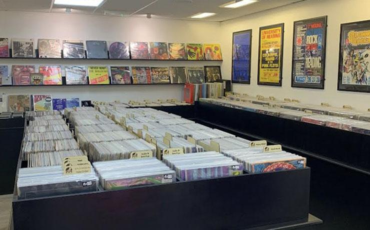An image of lots of vinyl with music related posters on the wall. 