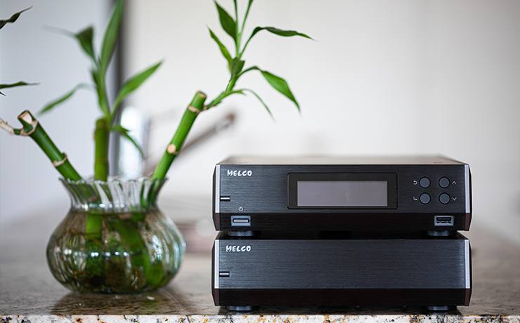 Melco N10/2 Digital Music Library in black.  Two boxes, one on top of the other on a granite table with a glass vase beside it.  In the vase are sprouting bamboo canes