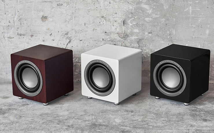 A trio of Audiovector QR Subs on a grey splattered style floor.  From right to left: dark walnut, white silk and piano black.