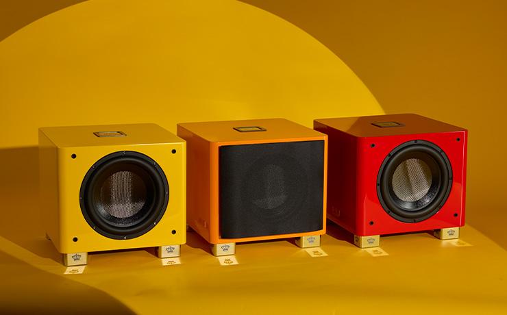 the three colours of the REL T/9x special edition subwoofer.  Yellow on the left, orange (with grille) in the middle and red on the right