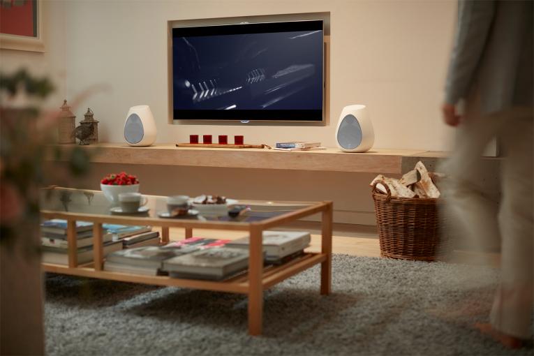 A Linn Series 3 302 wireless loudspeaker one side of a tv with a 301 the other side in a living room with a coffee table in the foreground.