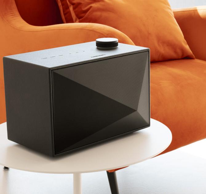 A black Astell & Kern ACRO BE100 Home Audio-Speaker on a small table beside an orange chair