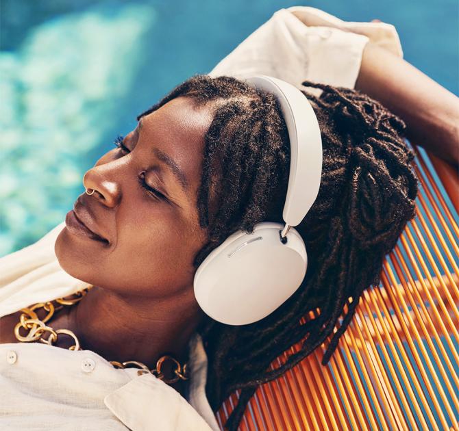 Sonos Ace Headphones in white on the head of a woman who is laying beside a swimming pool