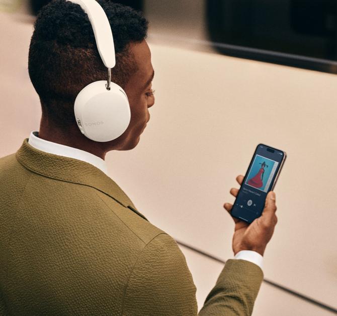 Sonos Ace Headphones in white on the head of a man holding his phone