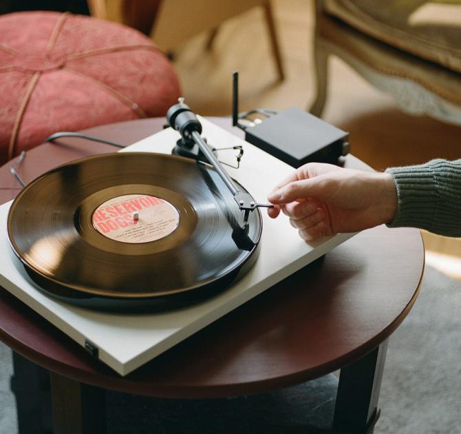 Project E1 Turntable on a small table with a person's arm reaching over and putting the needle on the record