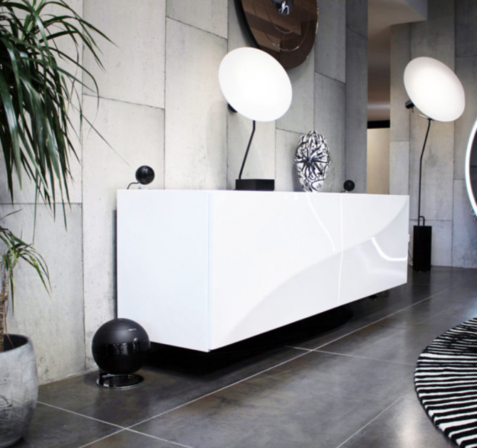 Cabasse Pearl Keshi Loudspeaker System in black in a modern living area.  The floor and walls are tiled.  there's a large indoor plant in a stone pot to the left.  